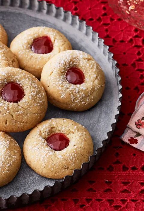 pioneer woman almond raspberry thumbprint cookies dusted with powdered sugar and filled with bright raspberry jam on a cooling rack