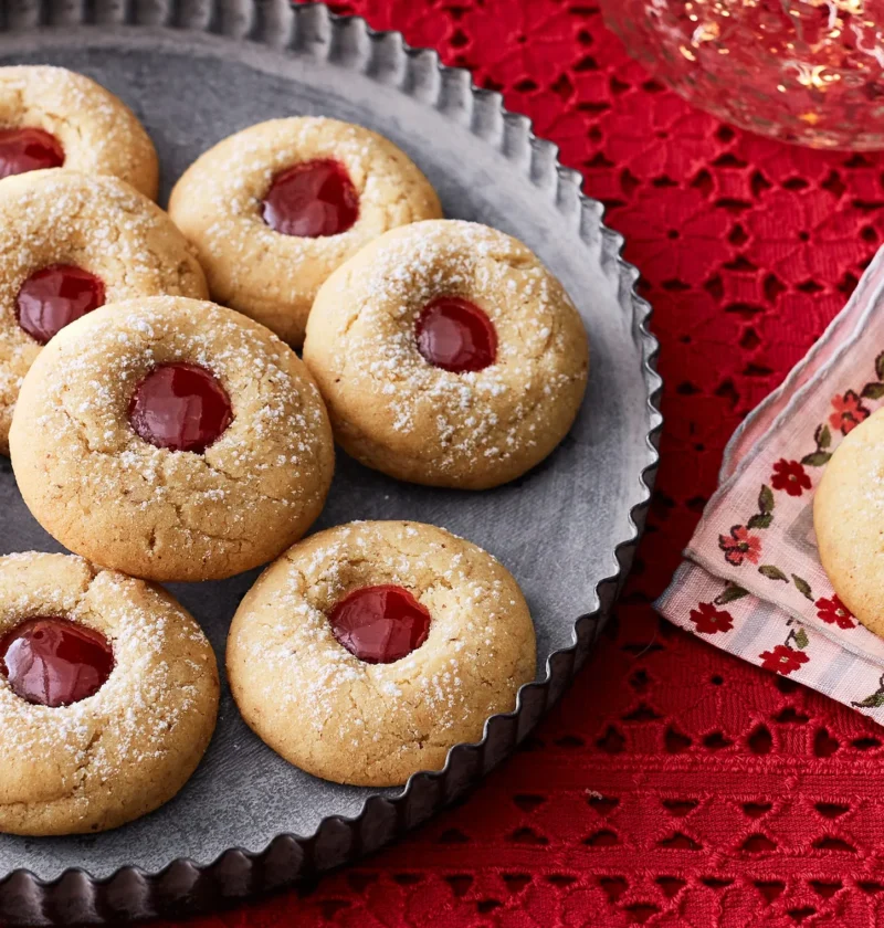 pioneer woman almond raspberry thumbprint cookies dusted with powdered sugar and filled with bright raspberry jam on a cooling rack