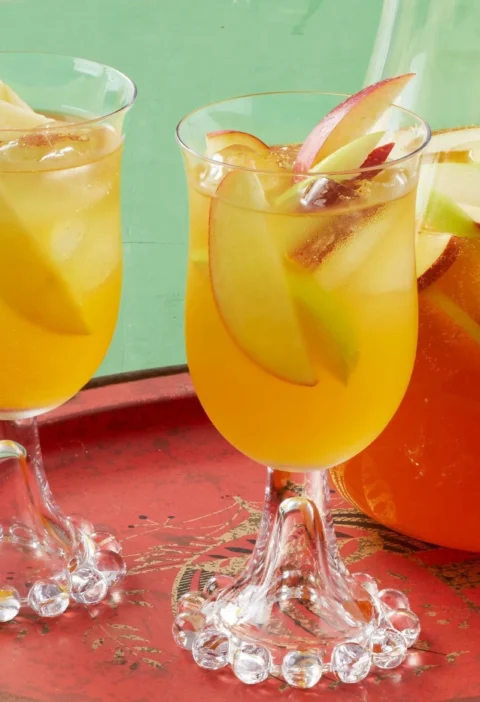 Pioneer woman apple cider sangria in a glass pitcher with thin apple slices floating in a golden cider and white wine mixture