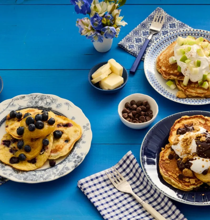 A stack of golden brown apple cinnamon pancakes topped with whipped cream and diced apples on a plate