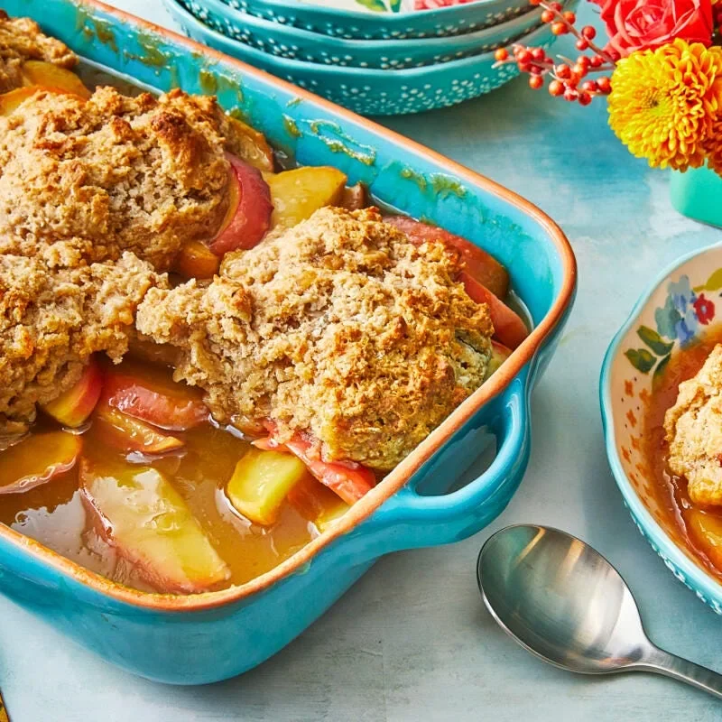 A baking dish filled with pioneer woman apple cobbler topped with golden drop biscuits and turbinado sugar
