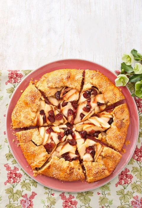 A golden-crusted apple cranberry galette with folded pastry edges and bubbly fruit filling on a baking sheet