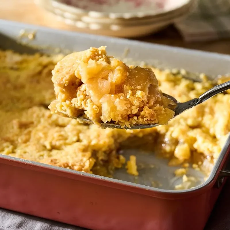 A golden brown apple dump cake in a baking dish with a buttery crispy crust, ready to serve with caramel sauce and ice cream
