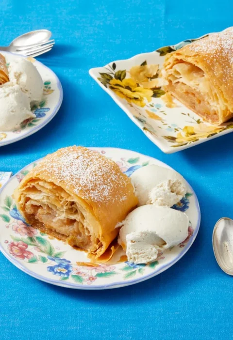 Flaky golden pioneer woman apple strudel dusted with powdered sugar on a baking sheet, filled with cinnamon apples and raisins