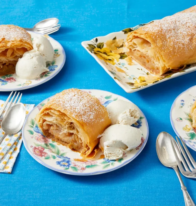 Flaky golden pioneer woman apple strudel dusted with powdered sugar on a baking sheet, filled with cinnamon apples and raisins