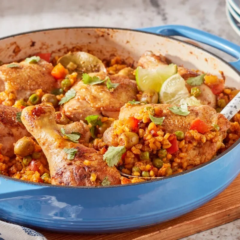 Arroz con pollo in a braiser with golden chicken thighs and drumsticks over saffron rice with peas and olives, a classic pioneer woman arroz con pollo dinner