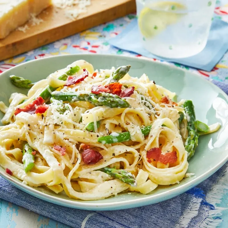 A plate of pioneer woman asparagus pasta with crispy bacon crumbles and grated parmesan on top of creamy fettuccine and green asparagus spears