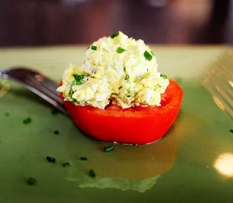 Pioneer Woman avocado egg salad scooped onto a thick red tomato slice on a green plate with chopped chives