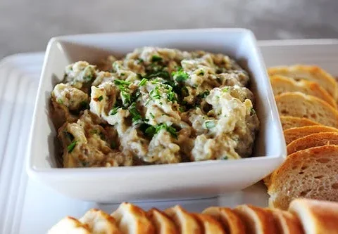 Pioneer woman baba ghanoush served in a white bowl with charred eggplant dip topped with olive oil and parsley