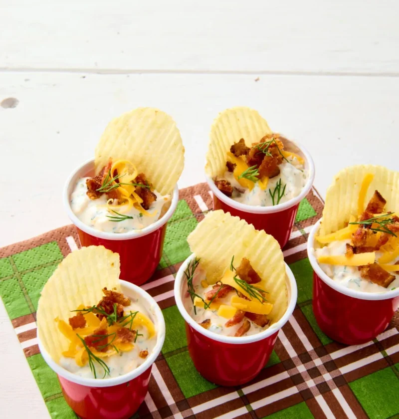 Bacon cheddar ranch dip served in small plastic cups topped with crispy bacon, shredded cheddar and fresh dill
