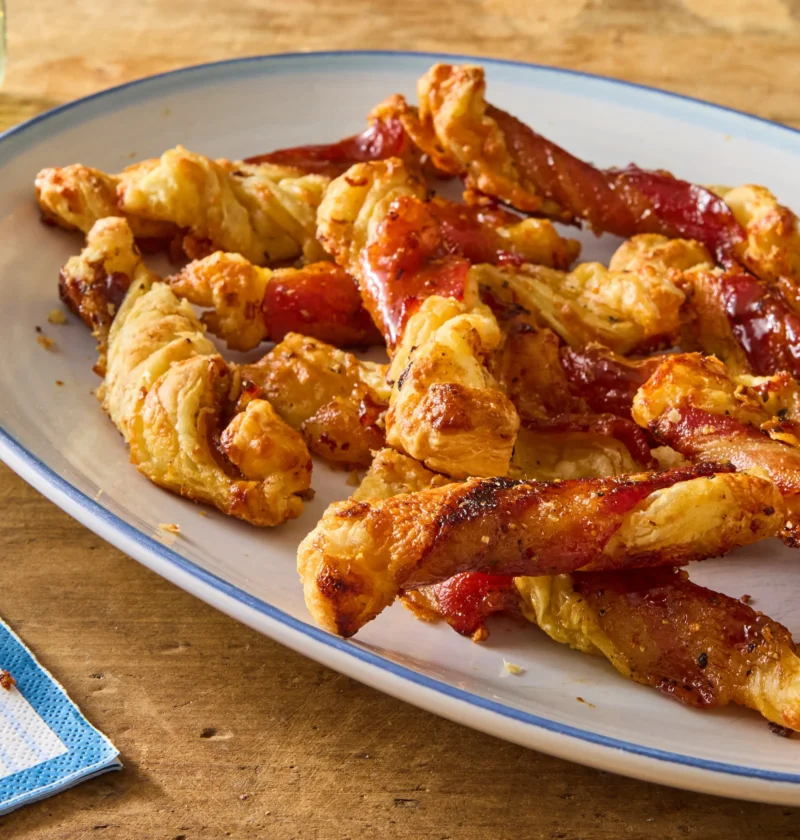 Bacon cheese straws twisted with candied bacon and melted cheddar on a parchment-lined baking sheet, a pioneer woman bacon cheese straws recipe
