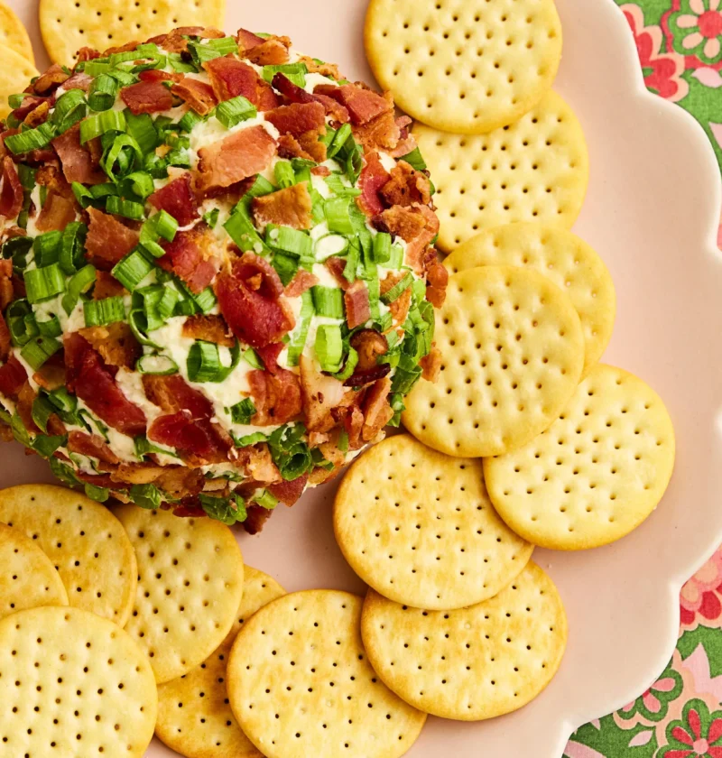 Bacon ranch cheese ball coated in crumbled bacon and sliced green onion greens served on a plate with crackers
