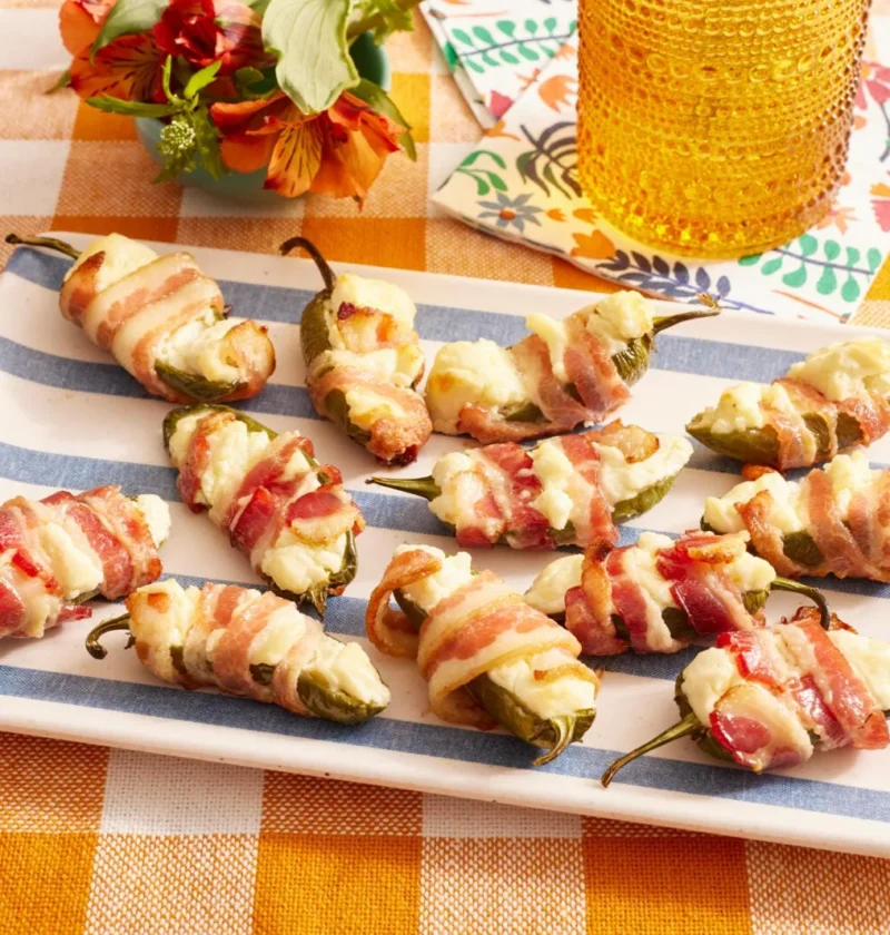 Bacon-wrapped jalapeno thingies lined up on a baking rack, each stuffed with cream cheese and wrapped in crispy bacon