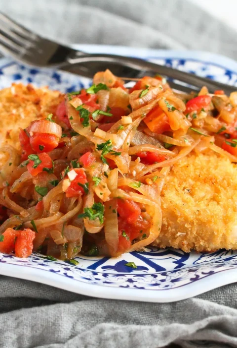 Baked crispy chicken with golden panko crust topped with caramelized onions and tomatoes on a plate