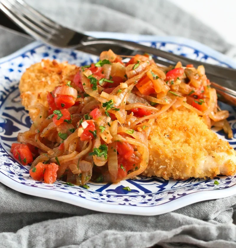 Baked crispy chicken with golden panko crust topped with caramelized onions and tomatoes on a plate