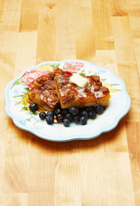 Baked French toast casserole in a white baking dish topped with golden brown cinnamon streusel and fresh blueberries