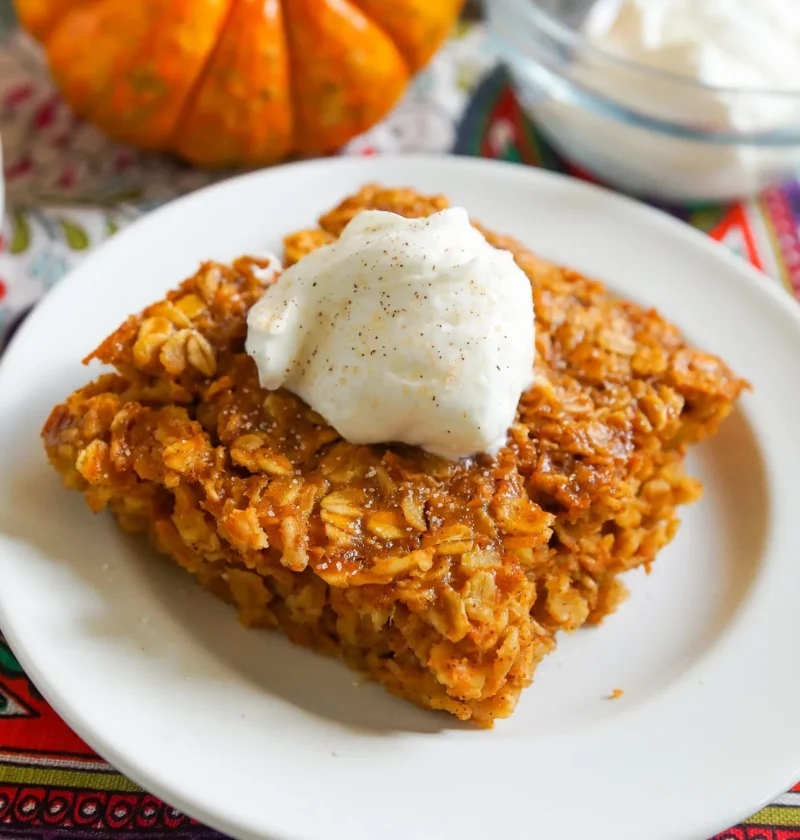 Baked pumpkin oatmeal sliced into squares in a baking pan, showing the golden brown top studded with oats and warm spices