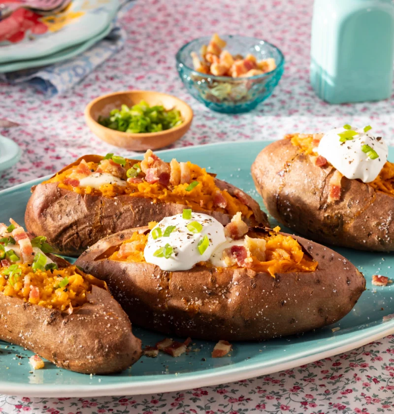 Baked sweet potato split open on a plate showing the fluffy orange interior with a pat of butter on top