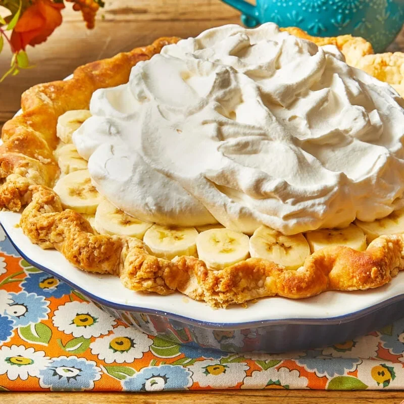 Pioneer Woman banana cream pie topped with whipped cream and sliced bananas in a deep-dish pie plate