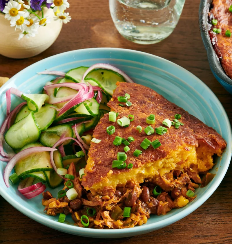 Cast iron skillet filled with pioneer woman BBQ chicken cornbread bake showing golden cornbread topping with melted cheddar and green onions
