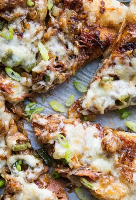 BBQ pulled pork pizza topped with caramelized onions, diced jalapenos, pepper jack and smoked mozzarella on a baking sheet